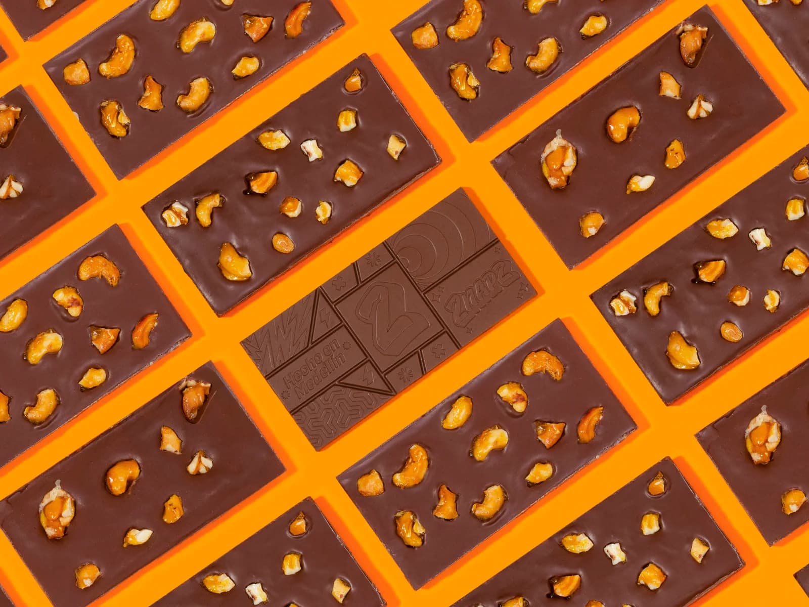 Cashew bars from the back, with cashews showing, around one bar with the molded “Hecho en Medellín” front, on an orange background.